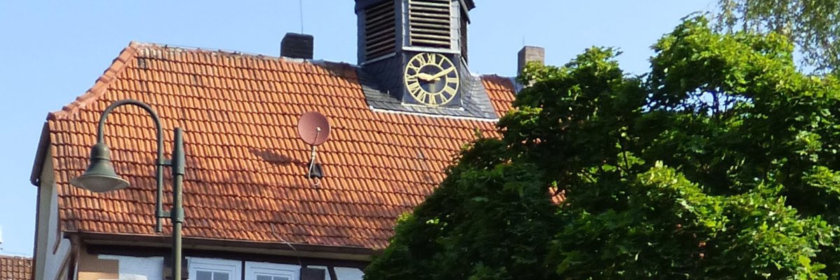 Fachwerkhaus mit Glockenturm hinter einem Baum